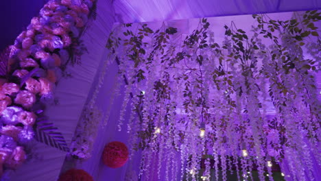 a vibrant indian wedding reception decor with hanging floral garlands and warm lights in slow motion