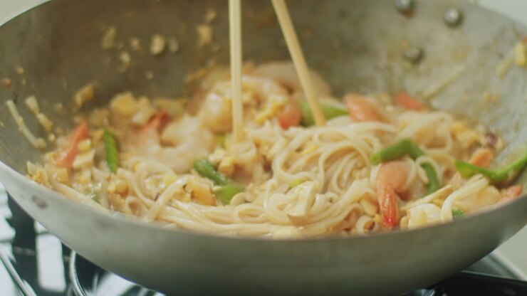 Donna che mescola noodles caldi nel wok con le bacchette.
