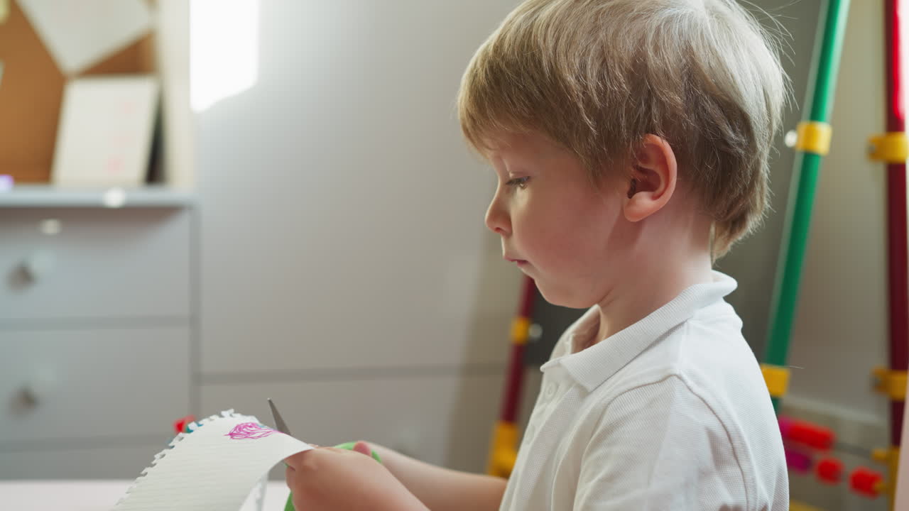 концентрированный маленький мальчик вырезает рисунок со страницы эскизной книги
