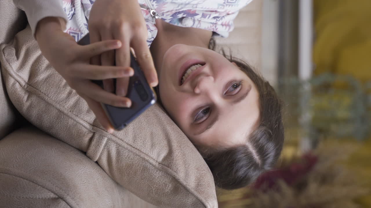 vídeo vertical de una mujer joven acostada en el sofá está usando el teléfono. postura agradable y cómoda.