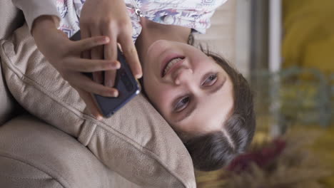 vídeo vertical de una mujer joven acostada en el sofá está usando el teléfono. postura agradable y cómoda.