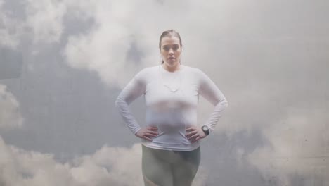animación de nubes sobre tamaño grande mujer caucásica en ropa deportiva flexionando los músculos
