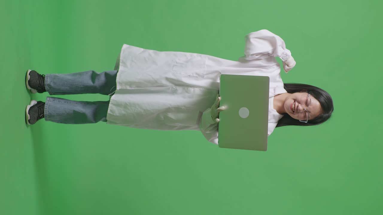 cuerpo lleno de mujer científica asiática mirando una computadora portátil y gritando meta celebrando mientras estaba de pie en el fondo de la pantalla verde en el laboratorio