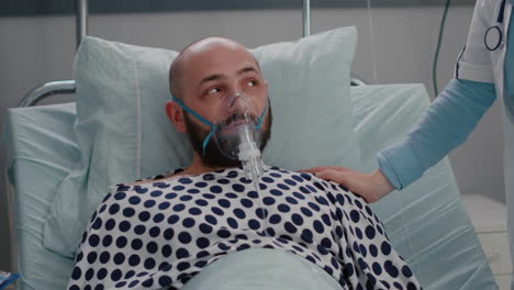 Close-up-of-sick-man-patient-resting-in-bed-while-doctor-putting-oxygen-mask