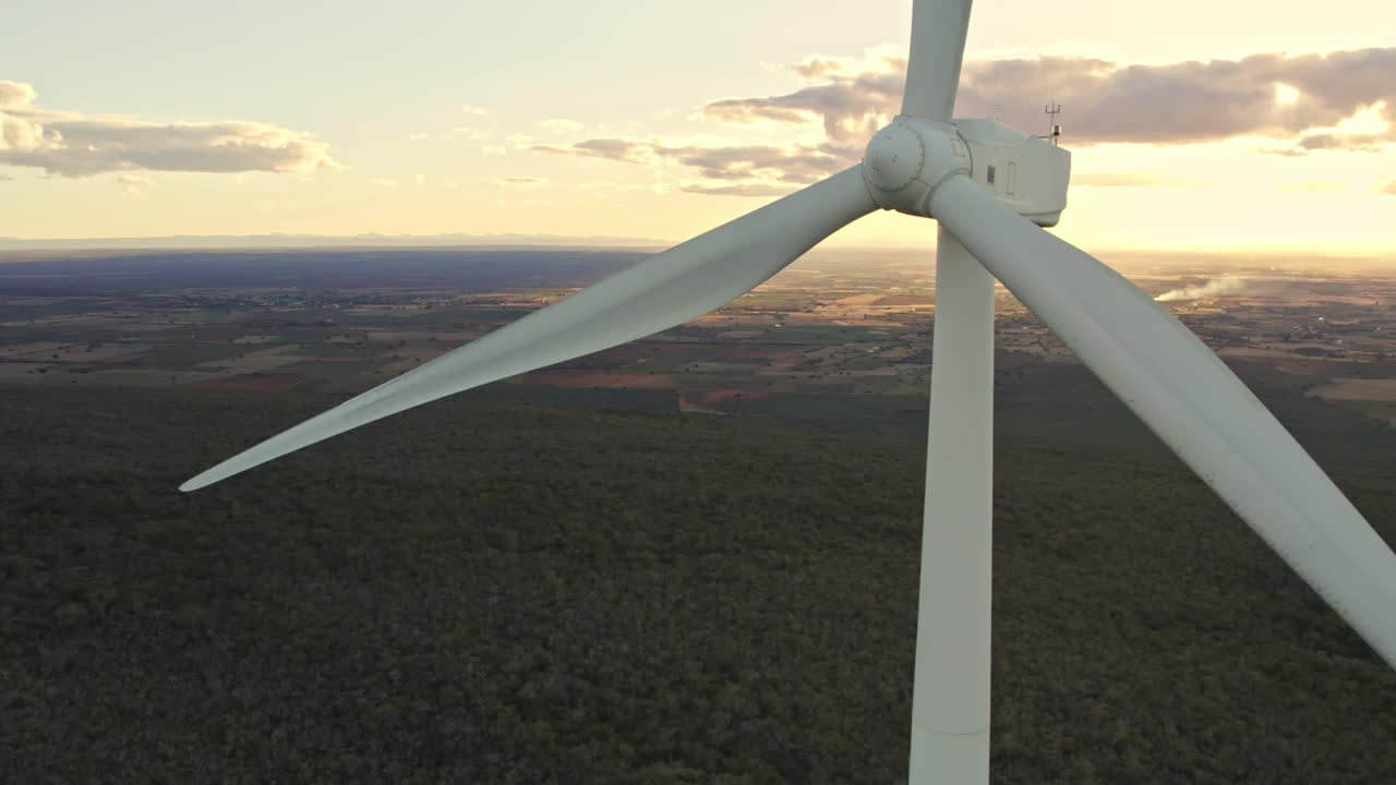 Close up aerial circling shot of wind turbine in operation during yellow sunset with clouds