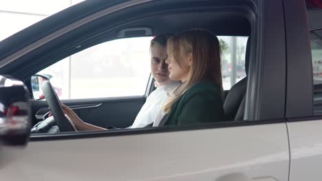 stylish man sitting in car salon and talking with female car dealer. professional helping client to choose best automobile in showroom