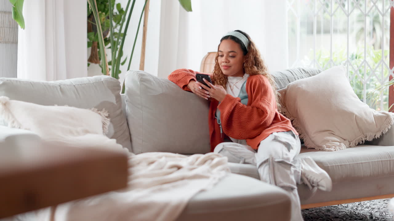 젊은 여성이 스마트폰을 사용하여 소파에서 휴식을 취하고 있습니다.