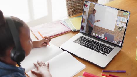 African-american-girl-using-laptop-for-online-lesson-with-caucasian-male-teacher-on-screen