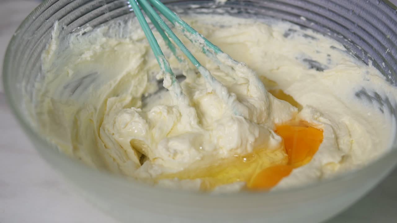 Close Up view of female hands preparing dough mixing eggs with other ingredients using whisk in the kitchen. Homemade bakery