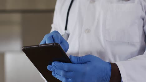 African-american-senior-male-doctor-wearing-white-coat-using-digital-tablet