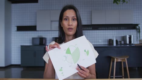 Mixed-race-businesswoman-having-video-chat-going-through-paperwork-in-office-kitchen