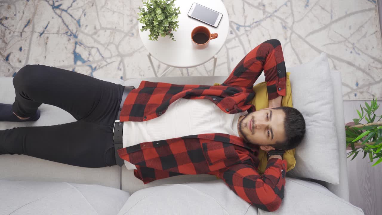 joven acostado solo en el sofá de su casa moderna y soñando despierto con el futuro.