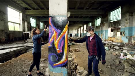 young people graffiti artists are using aerosol paint to decorate abandoned industrial building with modern graffiti images. creativity, street art and people concept.