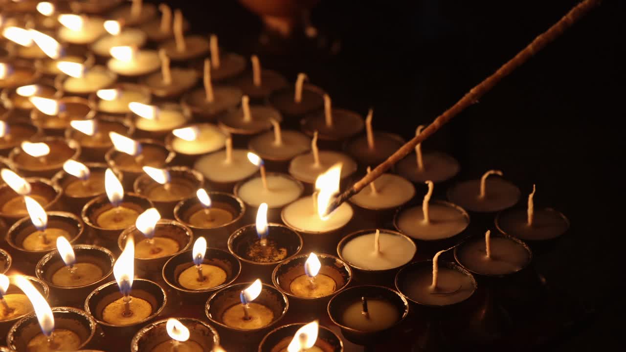 Primo piano dettagliato dell'accensione di lumini votivi simbolici con un accendino tradizionale in legno con stoppino, di notte