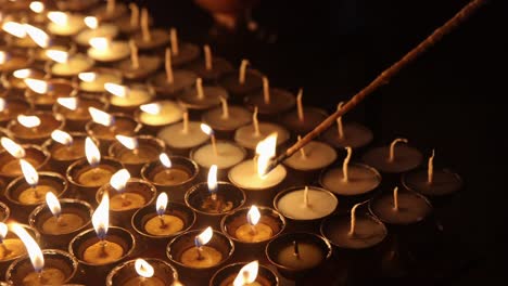 detailed closeup of lighting symbolic prayer tea light candles with traditional wick wooden lighter at night