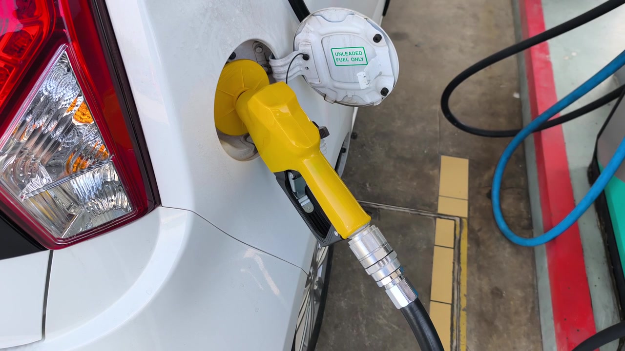 A fuel nozzle is inserted into a car gas tank to pump petrol. The vehicle gets refueled at a service station during a road trip.