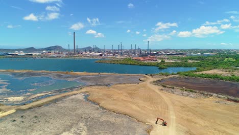 Maquinaria-Pesada-En-Un-Foso-De-Arena-Lleno-De-Lago-Asfáltico-De-Refinería-De-Petróleo-Al-Otro-Lado,-Curacao,-Drone