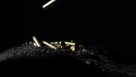 .22 long rifle bullets falling on gunpowder dust pile, black background, slowmo