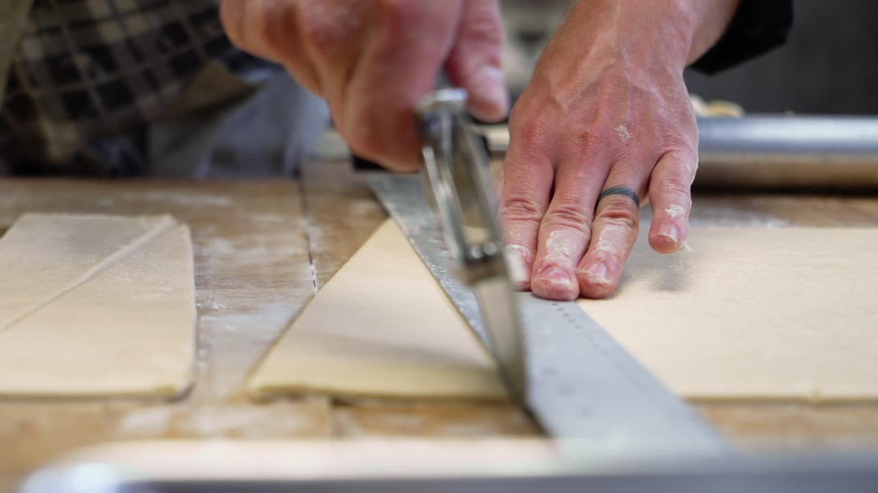 Baker maticulously measures and cuts triangle pieces of dough for croissants, slow motion close up 4K