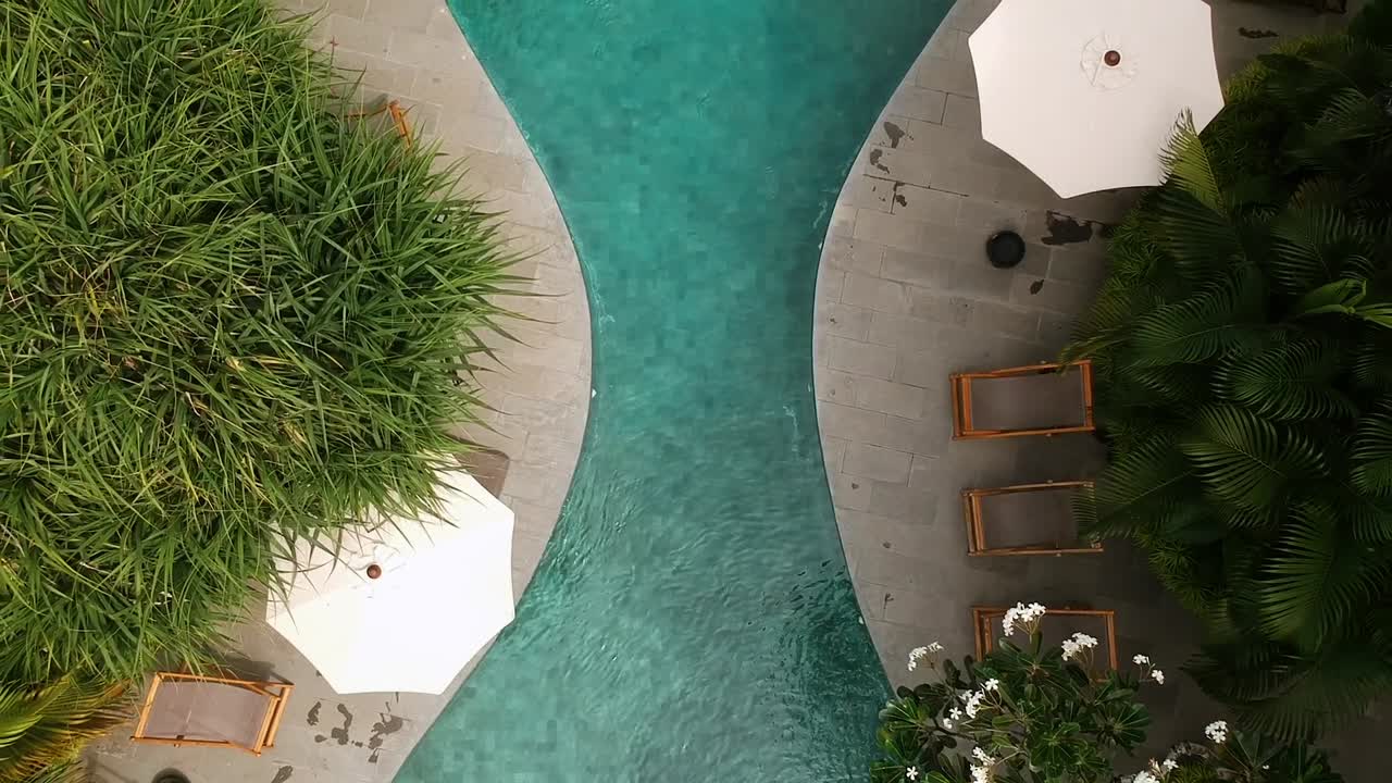 disparo de drone con vista de pájaro de arriba hacia abajo que revela una piscina en forma de reloj de arena en un lujoso resort ubicado en bali, indonesia