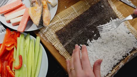 lady spreading rice all over with fork, preparing sushi roll, homemade