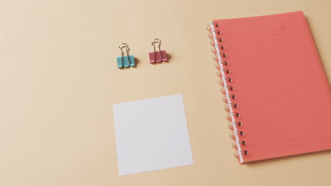 primer plano de un cuaderno rojo y artículos escolares dispuestos sobre un fondo beige, en cámara lenta