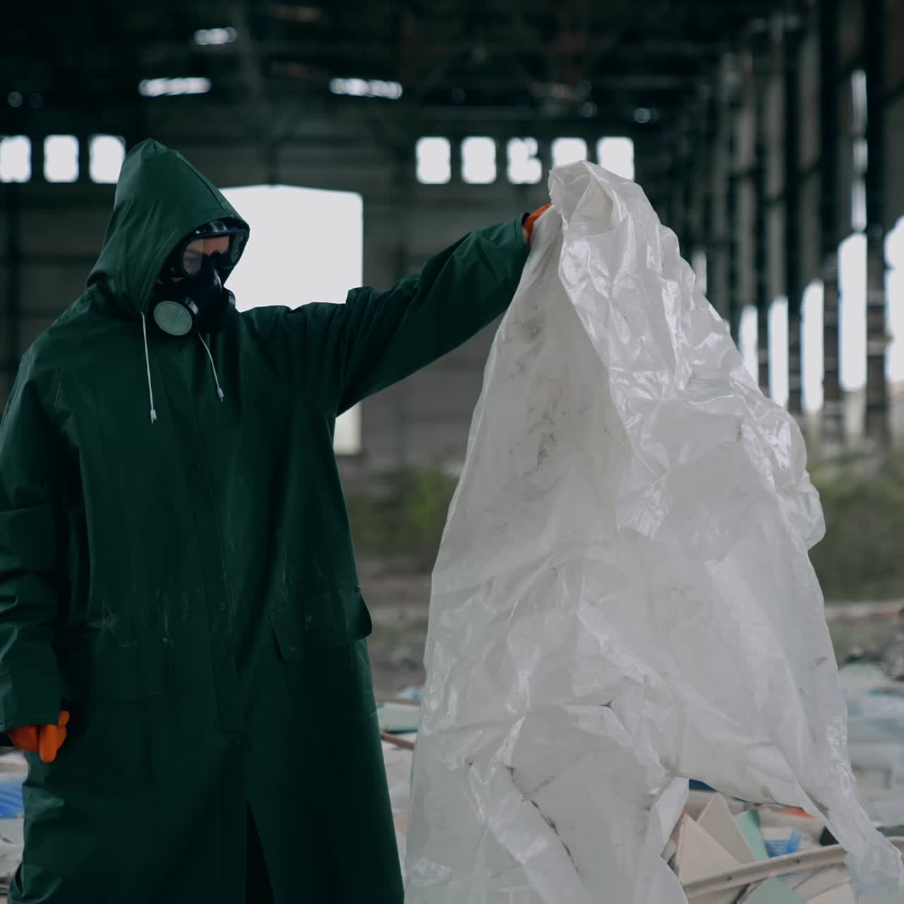 Scientist in abandoned place. Worker in protective suit and gas mask standing inside the ruined building with many garbage. Post-apocalyptic zone