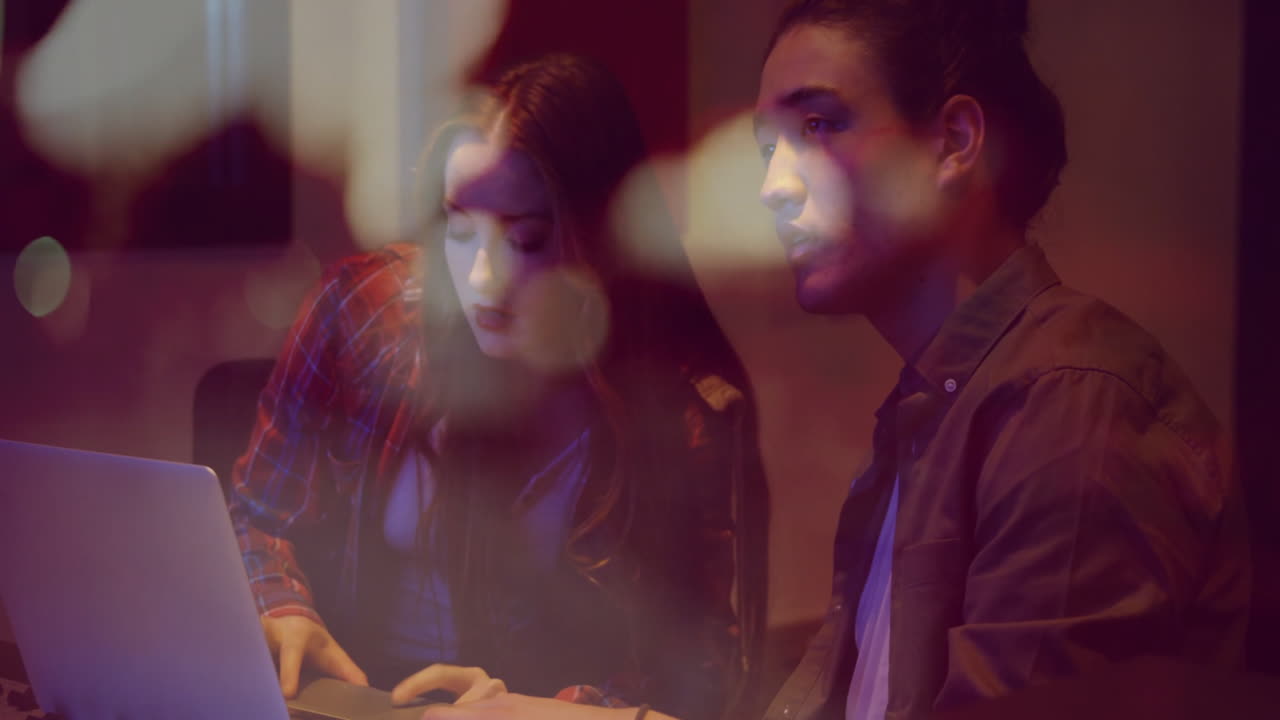 Coworkers typing on laptop in studio, displaying floating technology graphs around screen