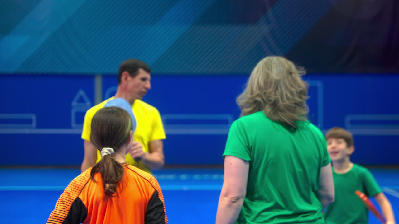 To voksne og to barn som slår hverandre high-five etter å ha spilt pickleball på en blå innendørsbane