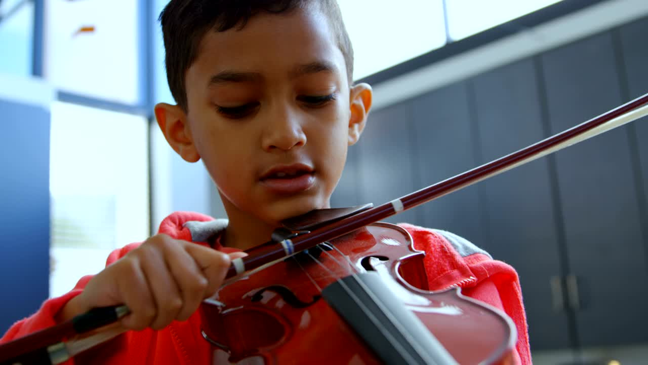 Front view of attentive Asian schoolboy playing violin in classroom at school 4k