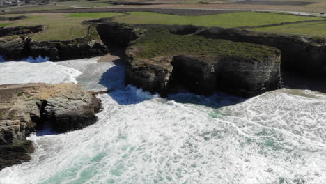 white foamy waves crashing on the rocky cliffs by the shore of playa das catedrales ocean in spain through summer. - aerial drone shot