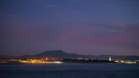 Cinematográfica-Maravillosa-Toma-De-Apertura-Dramático-Tarde-Noche-Anochecer-Luces-De-La-Ciudad-Faro-Biarritz-Hossegor-Francia-Playa-Montaña-Paisaje-Costero-Biarritz-País-Vasco-Aguas-Tranquilas-Bahía-Escénico