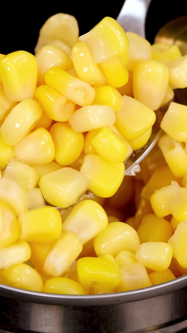 Une cuillère en métal soulève des grains de maïs doux jaune vif d'une boîte ouverte sous un éclairage de studio, avec des gros plans et un mouvement de caméra fluide.
