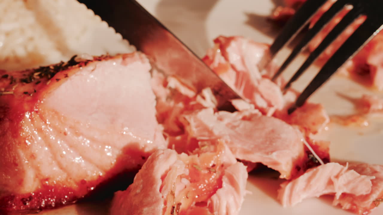 Close up of a fork and knife cutting into a a freshly grilled salmon fillet seasoned with herbs