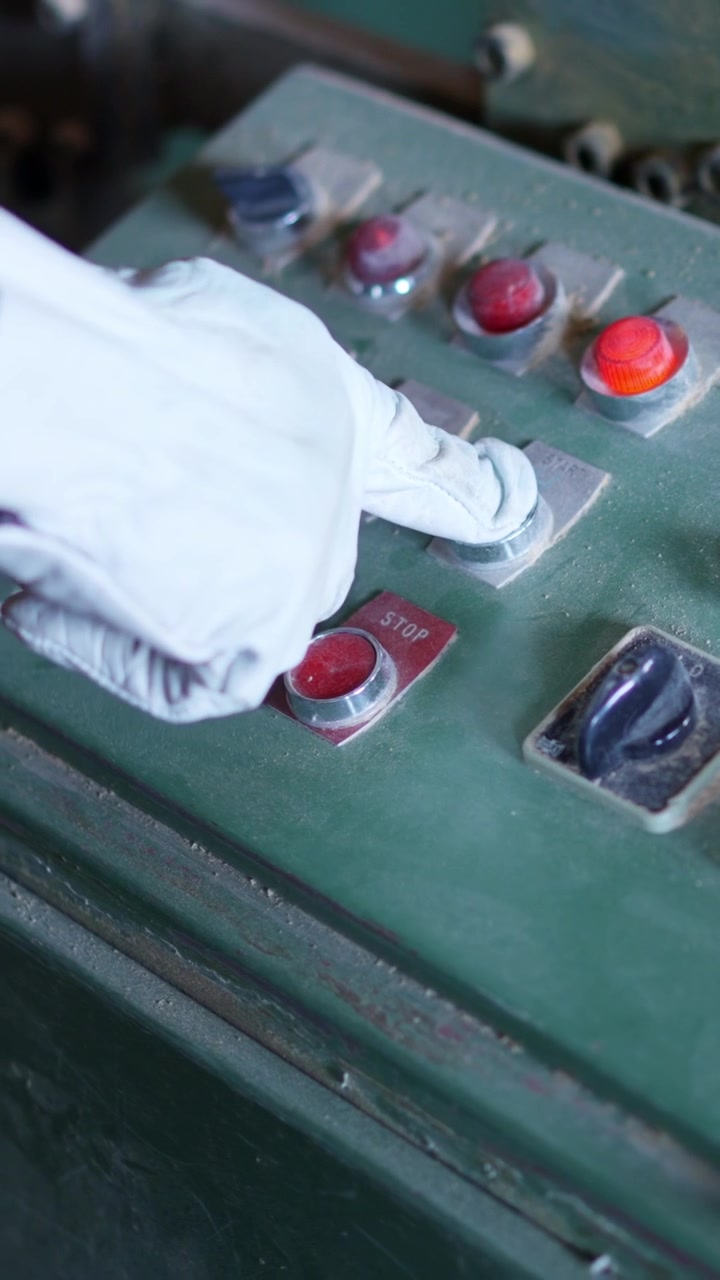 Gloved Hand Pressing Start Button on Dusty Industrial Control Panel