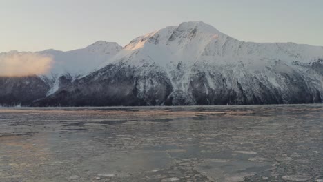 Impressive-mountain-peak-towers-high-above-calm-Cook-Inlet-in-Alaska,-aerial-pan