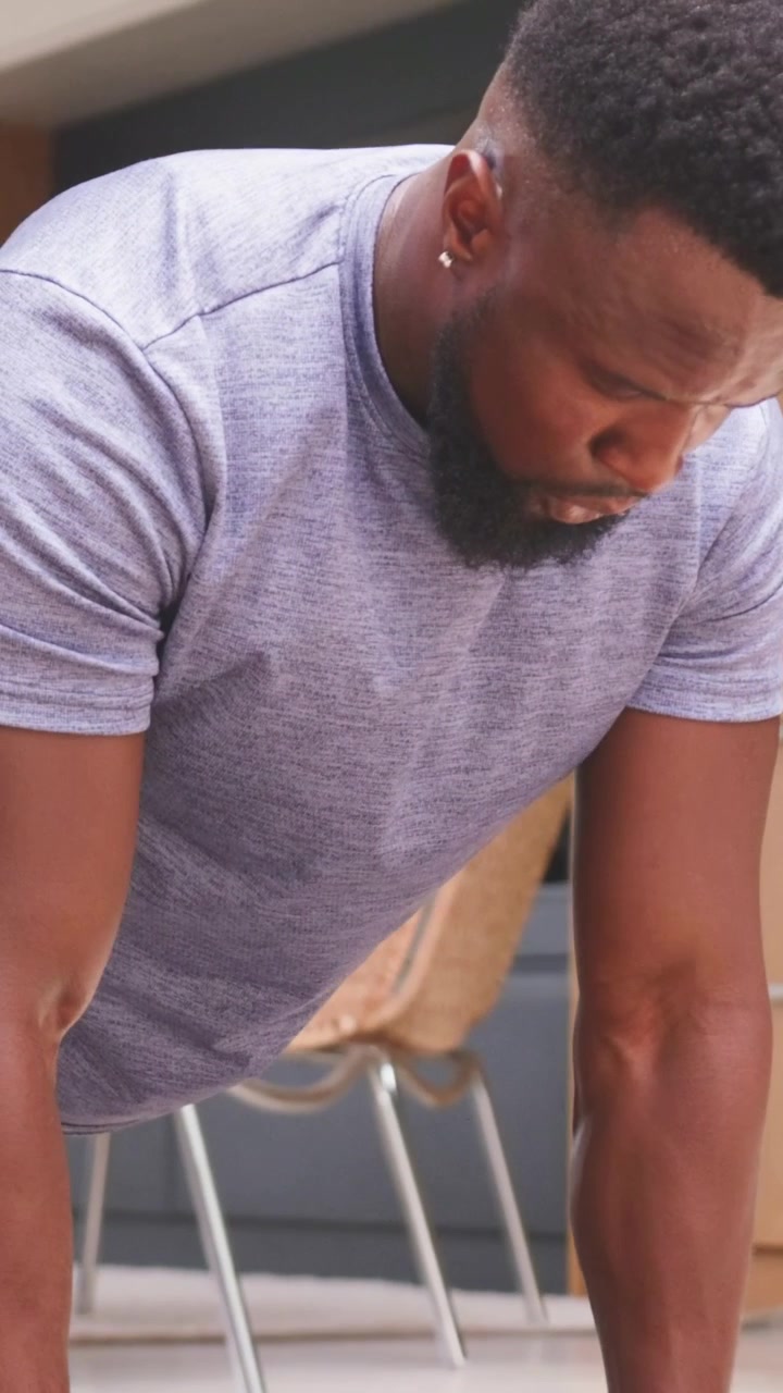 Vertical video: Man leaning forward gripping hex dumbbells doing push-ups on mat building fitness
