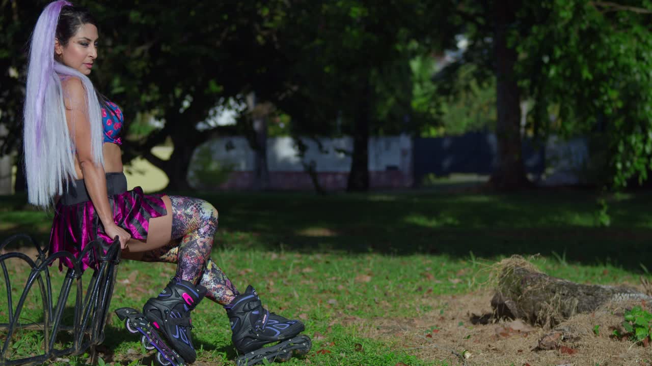 zoom de cerca de una mujer joven en una minifalda y patines sentado en una valla en el parque