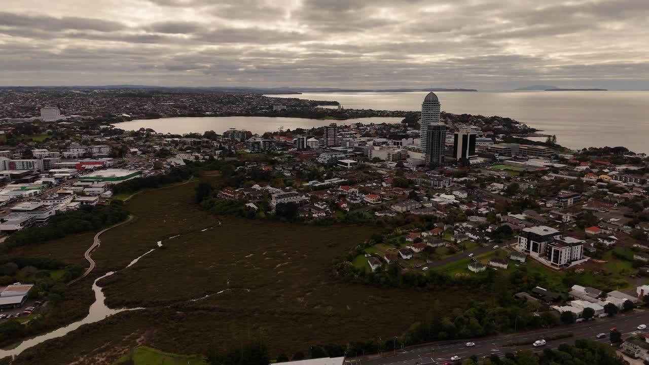 A stunning 4K 60fps aerial shot of Takapuna, a vibrant coastal suburb in Auckland. The footage showcases the famous beach, the town centre, and the iconic view of Rangitoto Island in the Hauraki Gulf