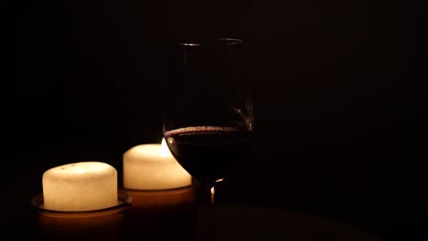 a glass of red wine in front of two burning candles