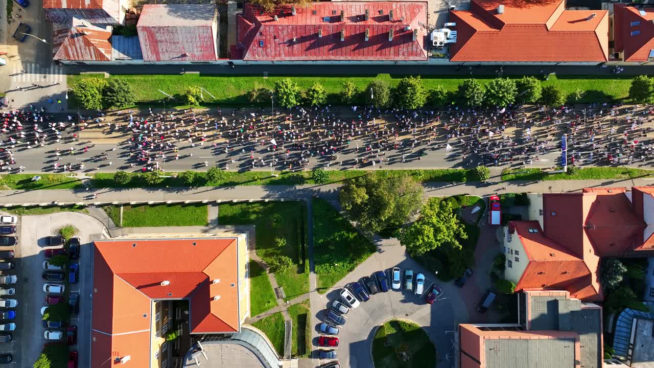 Aerial view of a large peaceful street protest, with participants marching between buildings, casting long shadows in the late afternoon sunlight. (4K)