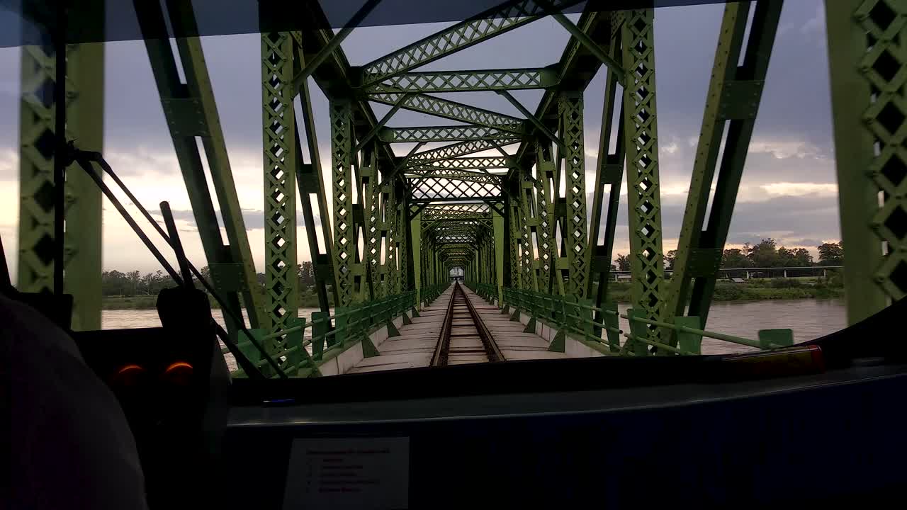 vista pov sobre el hombro de los conductores de tren mirando por la ventana delantera del tren mientras cruza la estructura del puente de metal verde