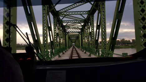 pov view over train drivers shoulder watching out of front train window as it crosses green metal bridge structure