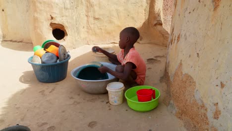 black african young child children kid washing dishes in remote rural village of africa poverty concept