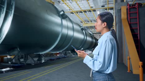 side view of asian business woman using mobile phone an looking around in pipe manufacturing factory