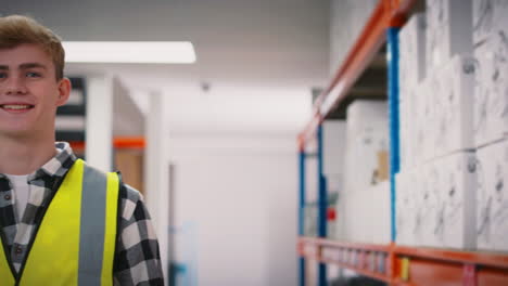 retrato de un joven trabajador sonriente con chaleco de seguridad de alta visibilidad sosteniendo una caja dentro del almacén
