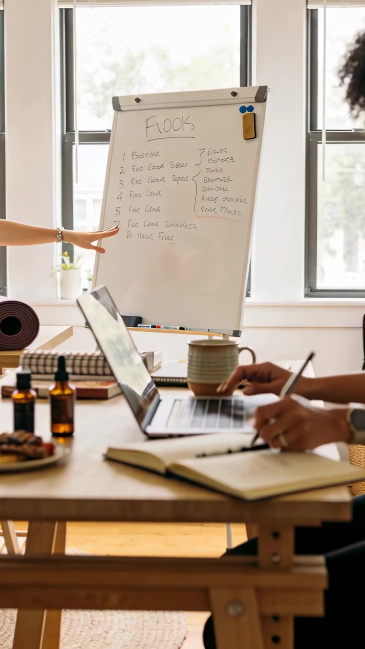 Vertical video: Typing she in longsleeve planning as peer pointing whiteboard at desk with laptop