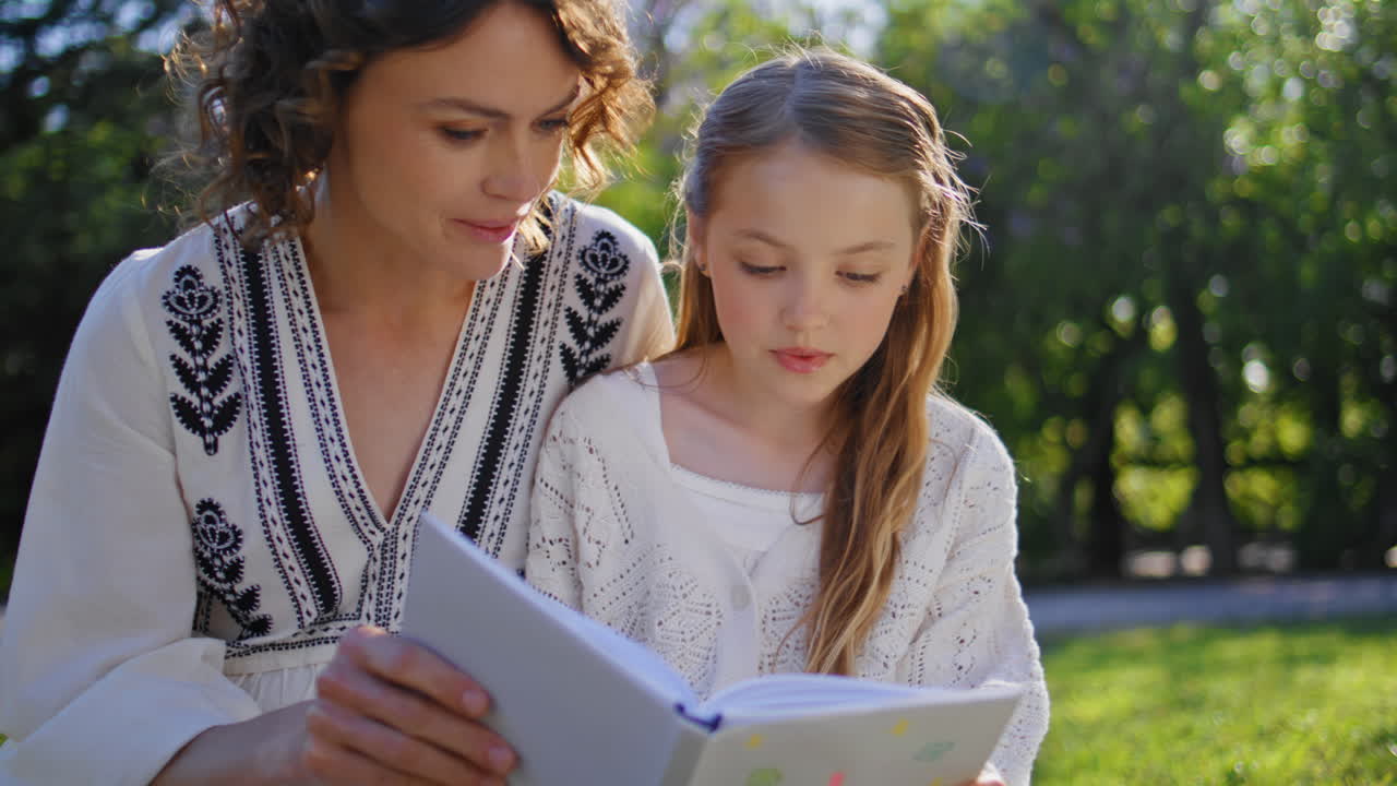 Nahaufnahme einer Frau und ihrer Tochter, die in der Natur sitzen und ein Buch lesen. Mutter und Kind entspannen sich