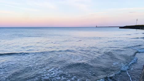 Ruhige-Wellen-Brechen-Sich-Bei-Sonnenuntergang-Am-Strand-Mit-Dem-Leuchtturm-Von-Roker-In-Der-Ferne