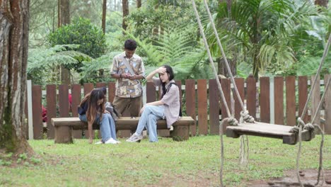 young asian indonesian friends sitting playing together on a wooden bench in forest park